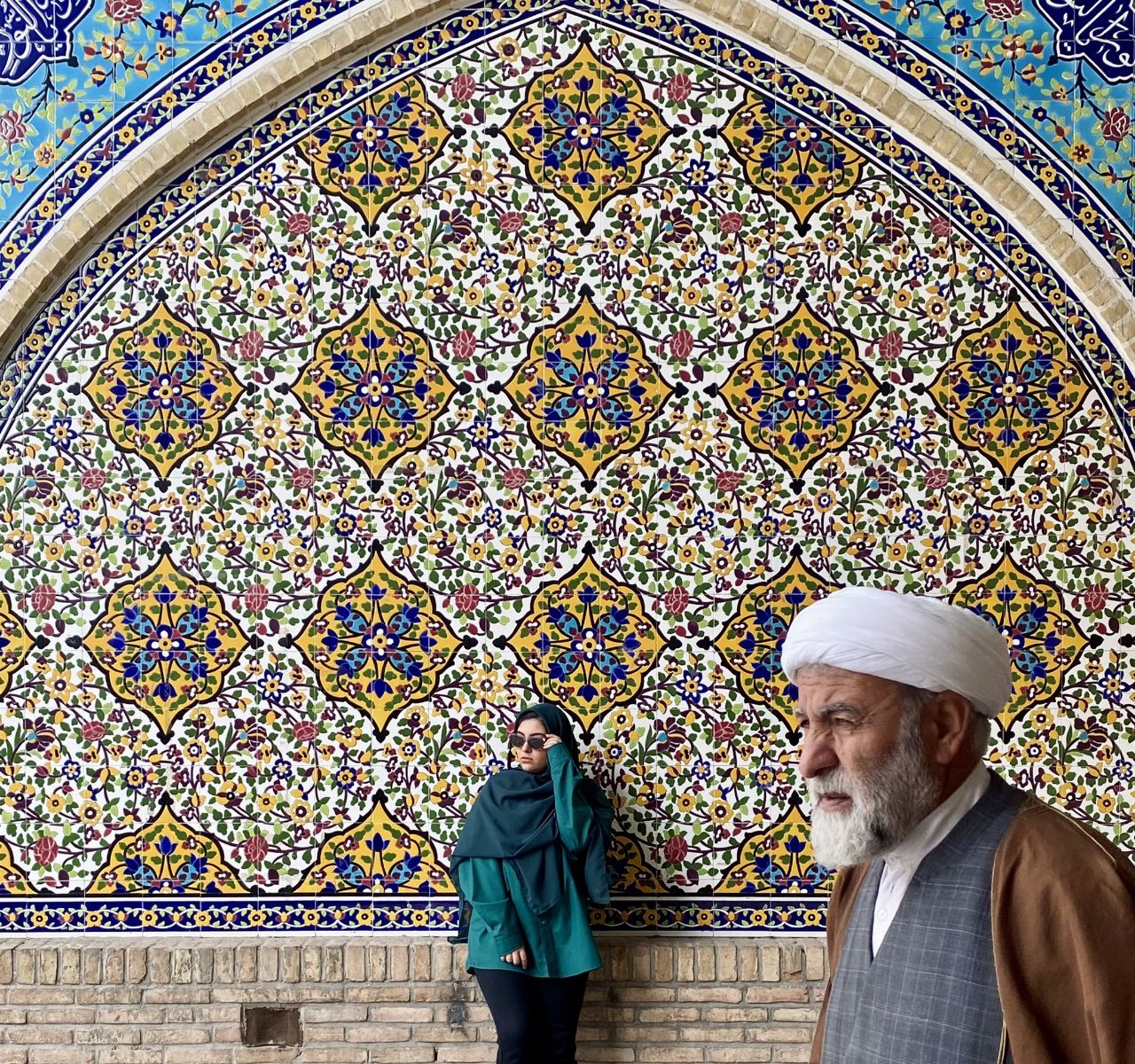 a man and woman standing in front of a wall with colorful tiles